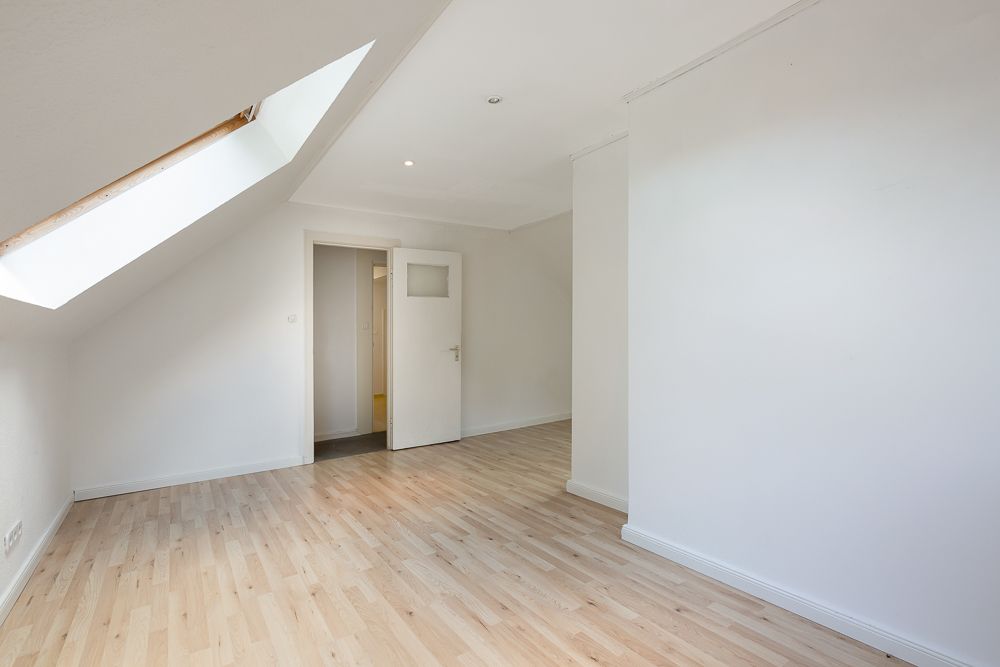 Heller leerer Raum mit Dachfenster, Holzboden und geöffneter Tür.