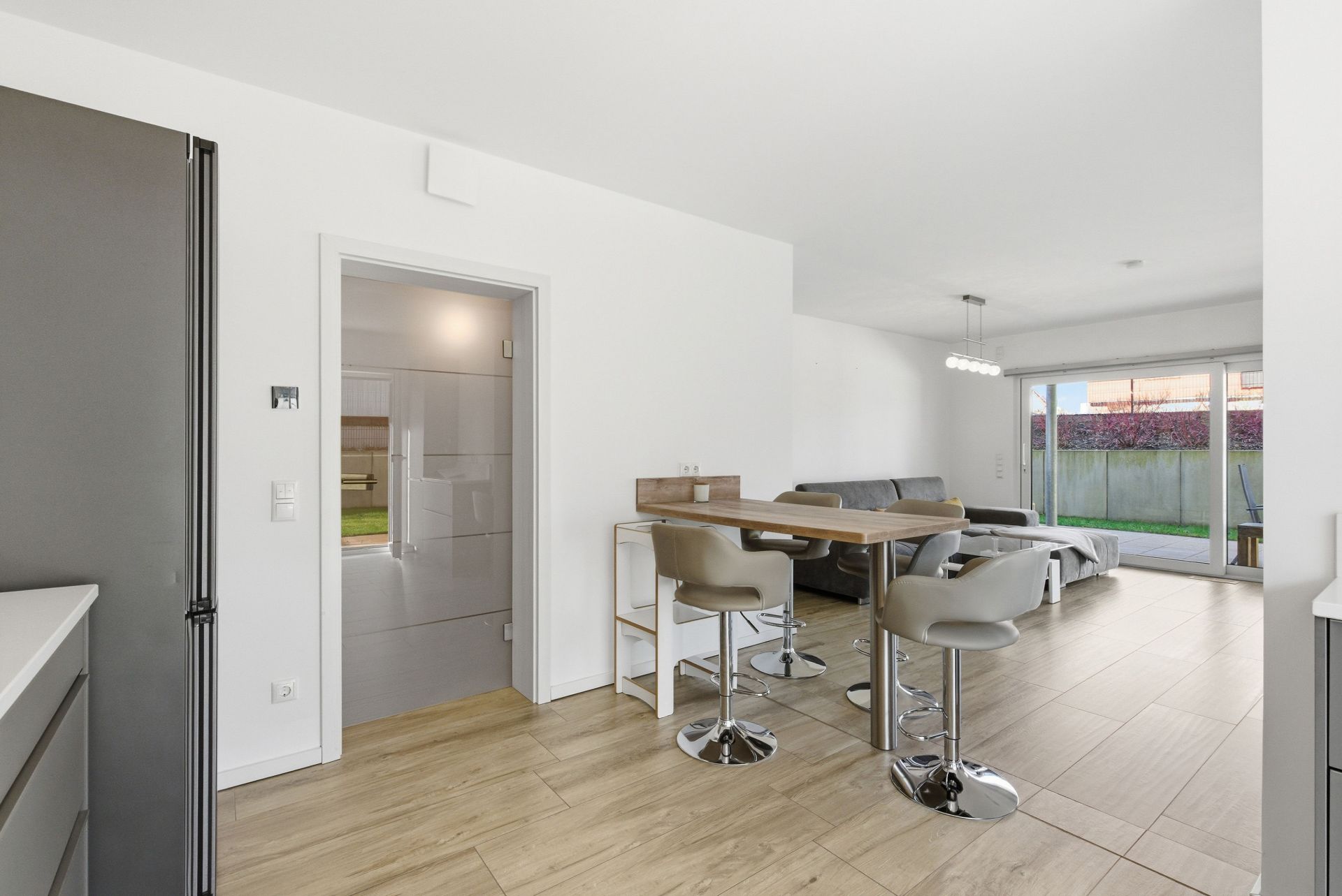 Moderner Wohn- und Essbereich mit Barstühlen, Sofa und großen Fenstern zum Garten.