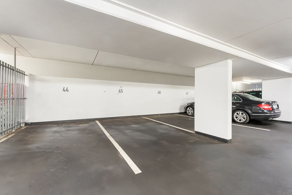Mehrere überdachte Parkplätze mit gemalten Linien, ein schwarzes Auto parkt rechts.