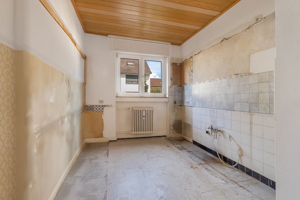 Leerer Raum mit Fliesen an der Wand, Fenster und sichtbaren Wasseranschlüssen.