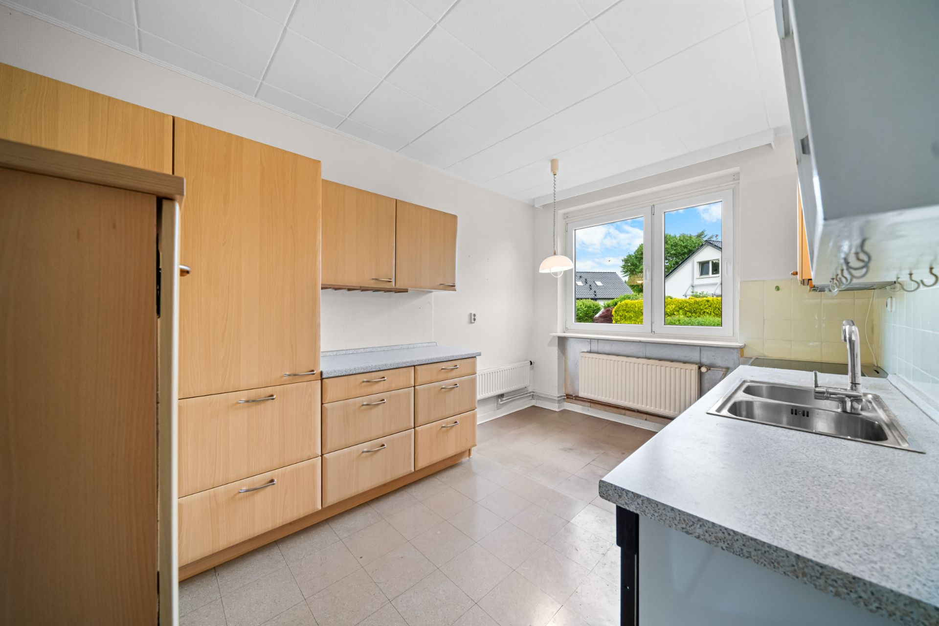 Helle Küche mit Holzschränken, großem Fenster und Spüle auf der rechten Seite.