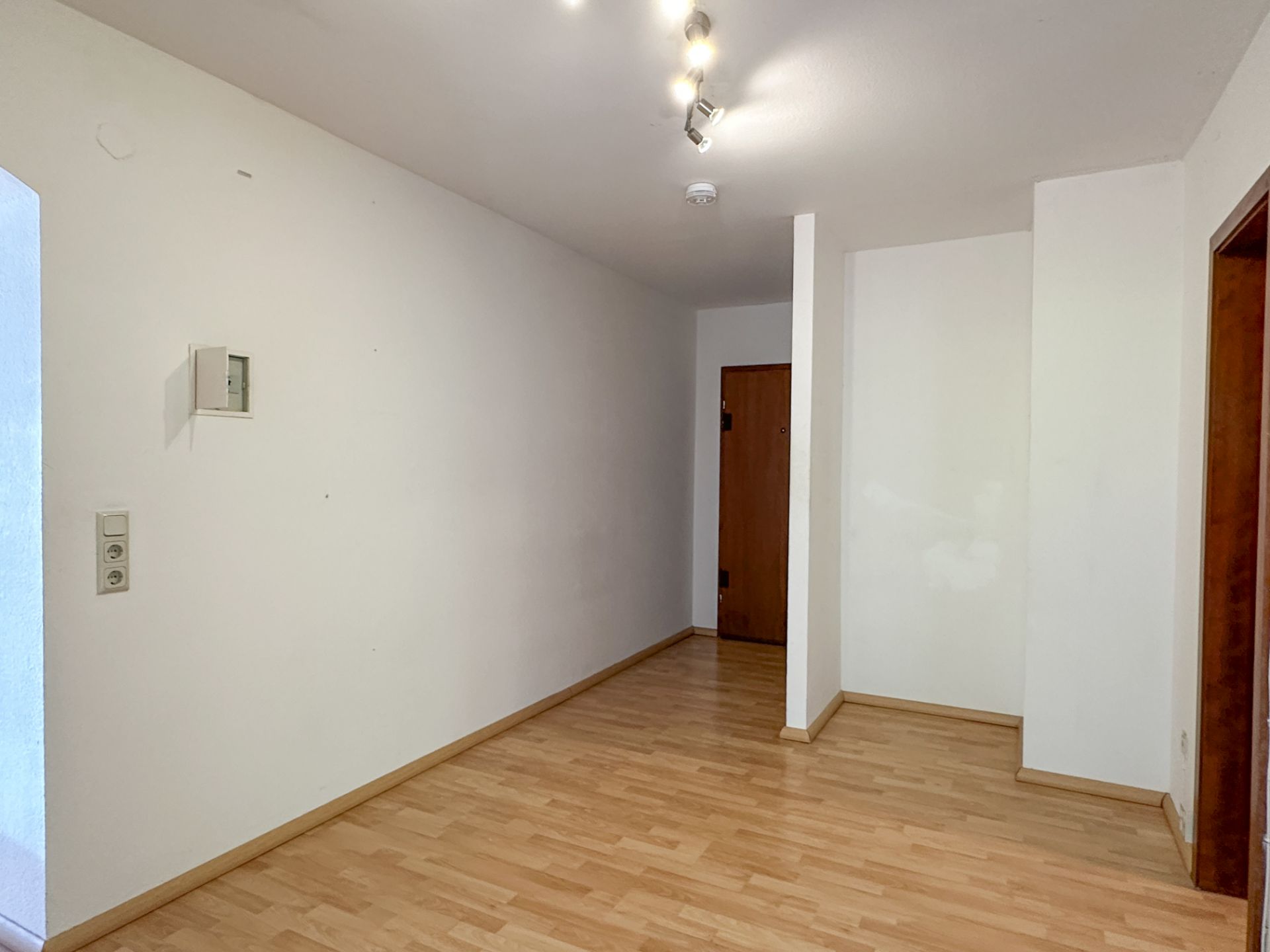 Heller Flur mit Holzfußboden, weißen Wänden und Deckenleuchte.