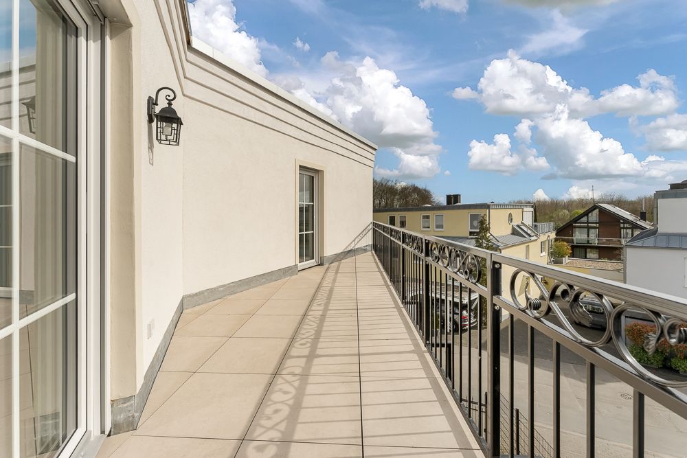 Großer Balkon mit Fliesenboden, Metallgeländer und Wandlampe an einer hellen Hauswand.