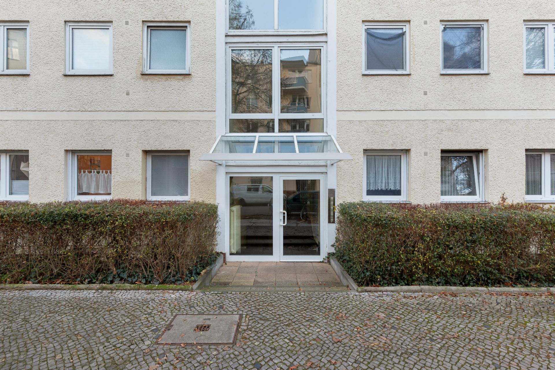 Eingang zu einem Mehrfamilienhaus mit Glastür und Büschen davor.