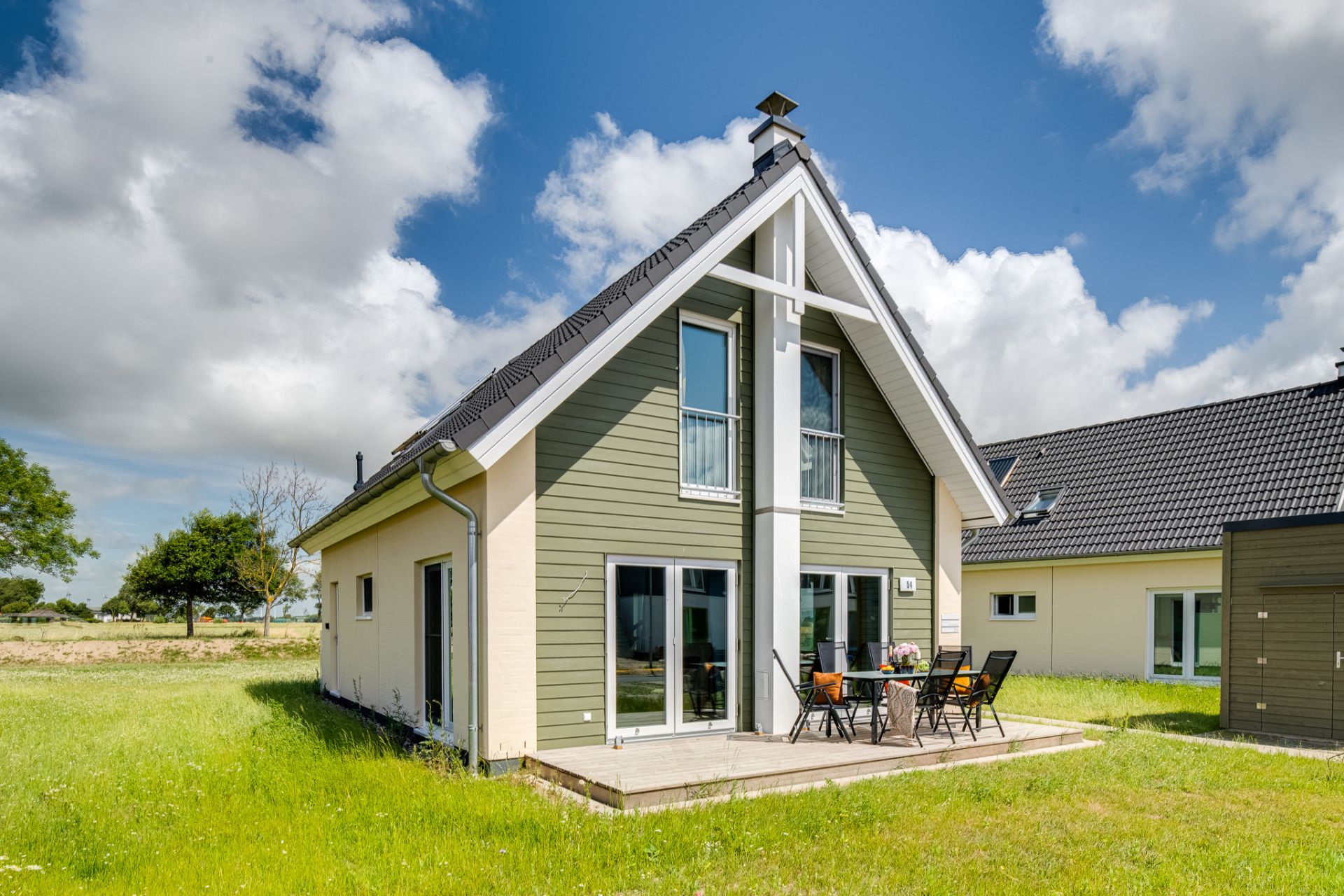 Modernes Einfamilienhaus mit Terrasse und Garten, Gartenmöbeln und großen Fenstern bei sonnigem Wetter.