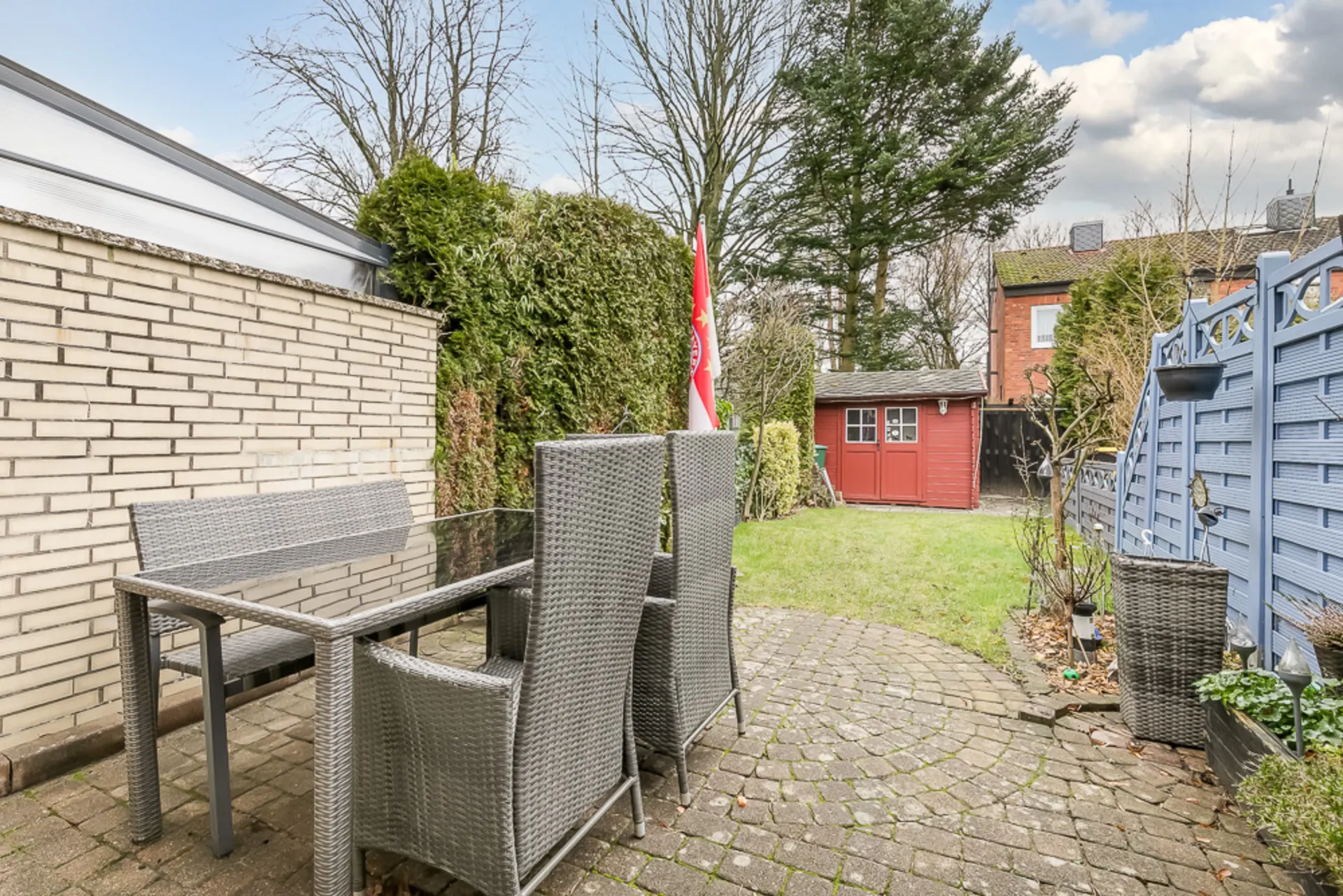 Garten mit Terrasse, Gartentisch, Stühlen und einem roten Gartenhaus im Hintergrund.