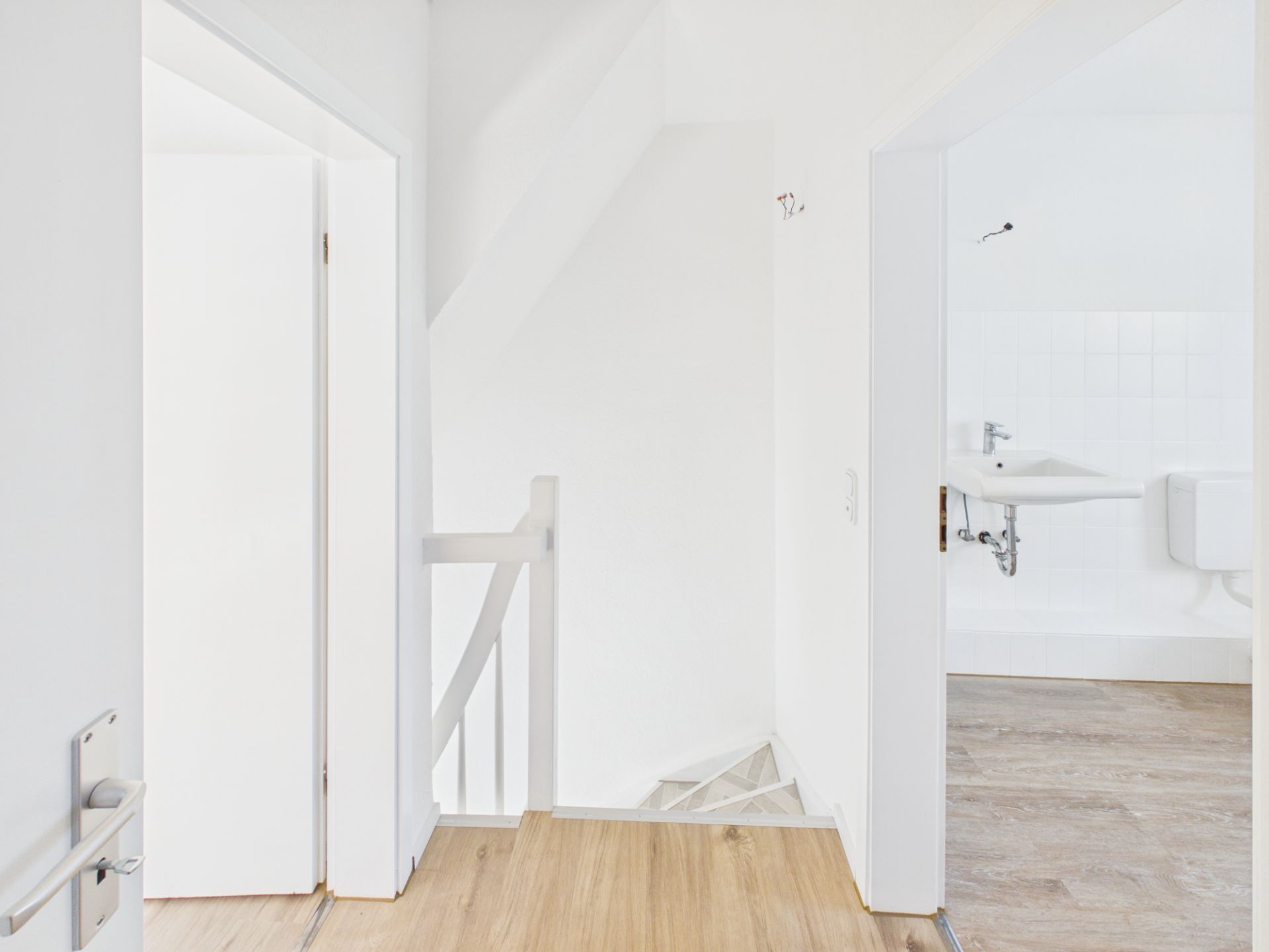 Heller Flur mit Holzboden, Treppe nach unten und Blick ins Badezimmer mit Waschbecken und WC.