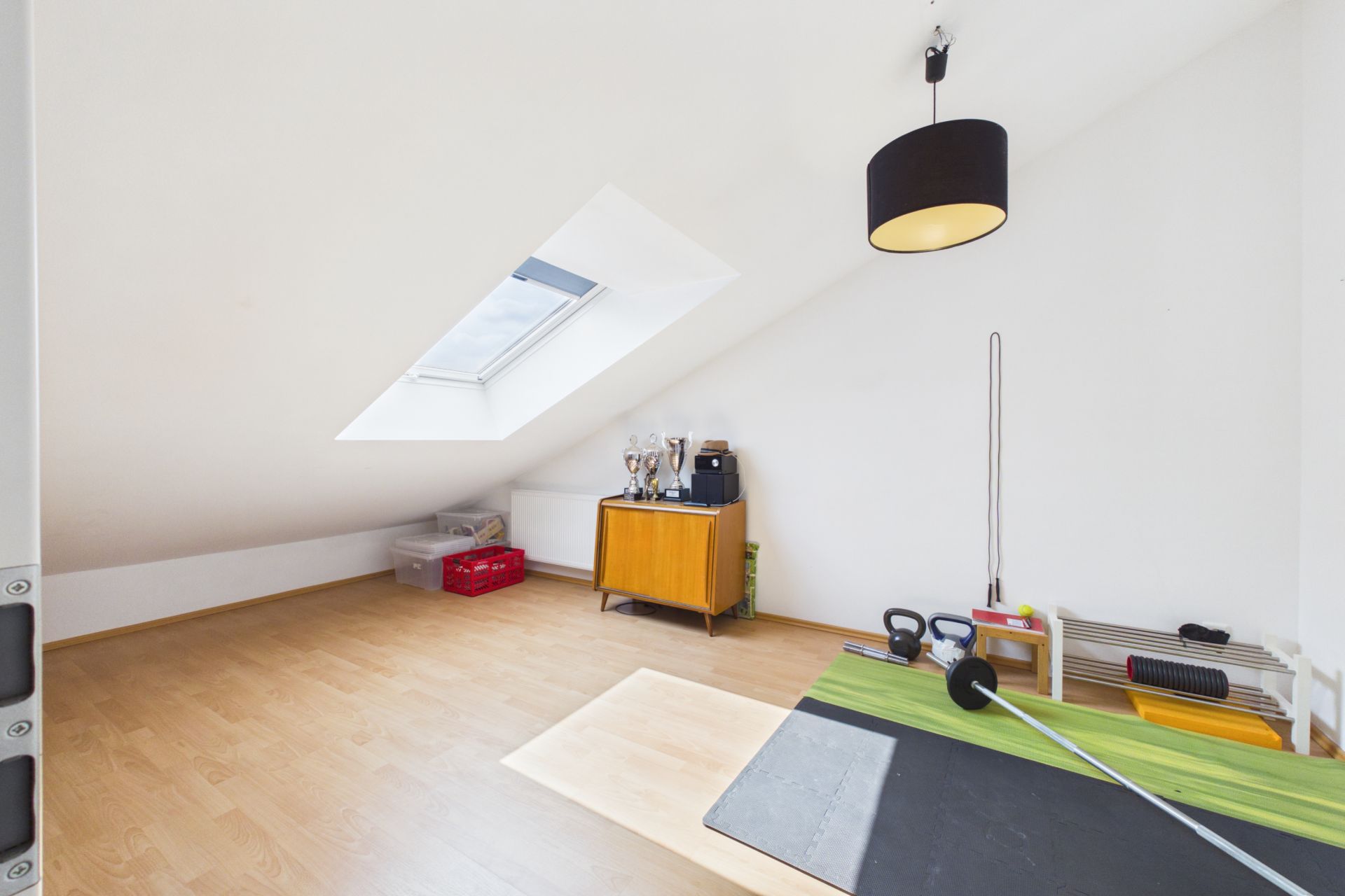 Heller Raum mit schräger Decke, Dachfenster, Holzfußboden und Fitnessgeräten.
