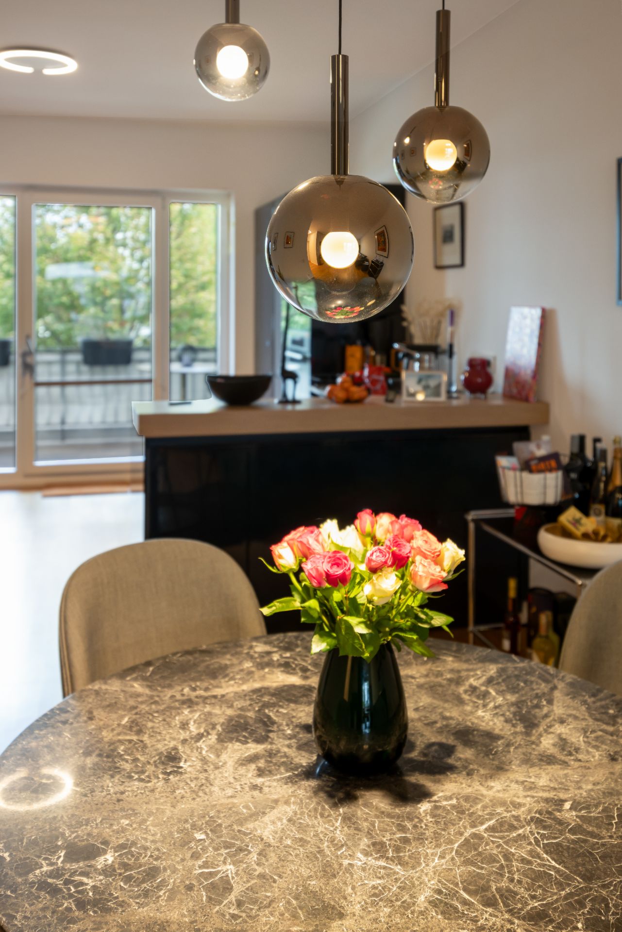 Runder Marmortisch mit Blumenvase, darüber drei moderne Hängelampen, im Hintergrund Küchenbereich.