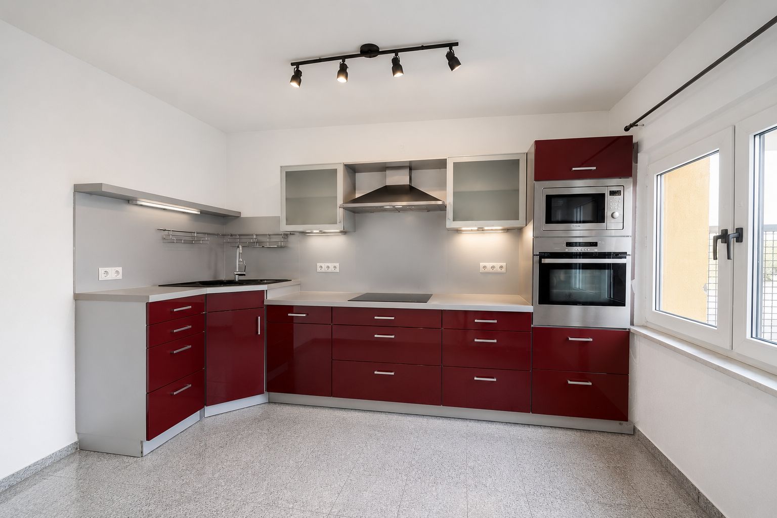 Moderne Einbauküche mit roten Schränken, Herd, Backofen und großem Fenster.