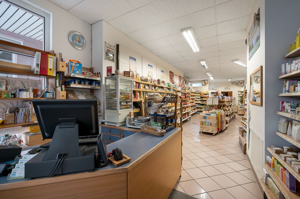 Verkaufsraum mit Kasse, Regalen voller Waren und gut beleuchtetem Fliesenboden.