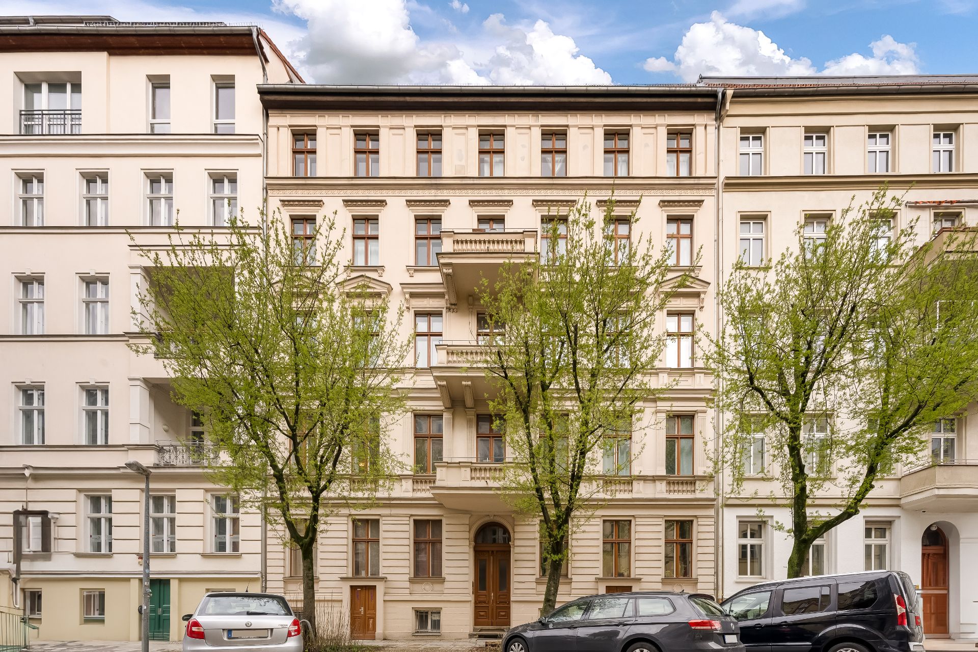 Mehrstöckiges Wohngebäude mit Bäumen und geparkten Autos davor.