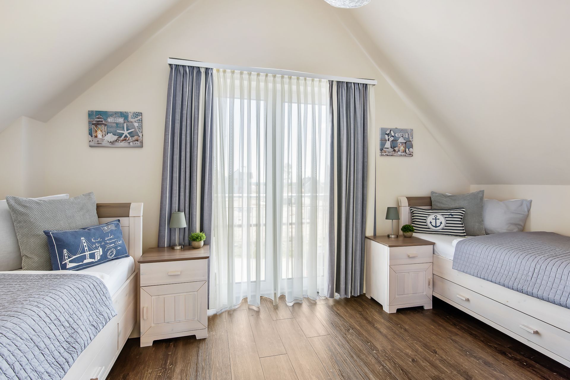 Helles Schlafzimmer mit zwei Einzelbetten, Holzboden und großen Fenstern mit Vorhängen.