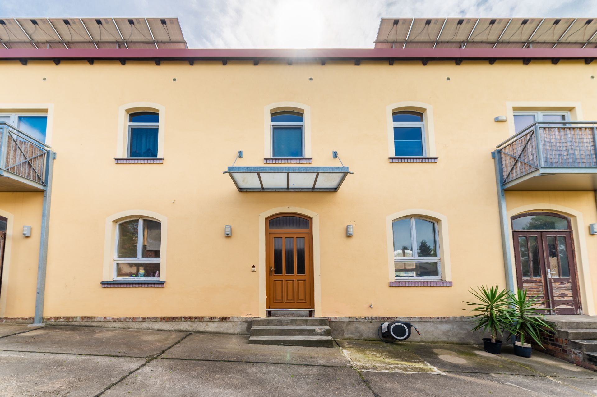 Zweistöckiges gelbes Wohnhaus mit brauner Tür, mehreren Fenstern und zwei Balkonen.