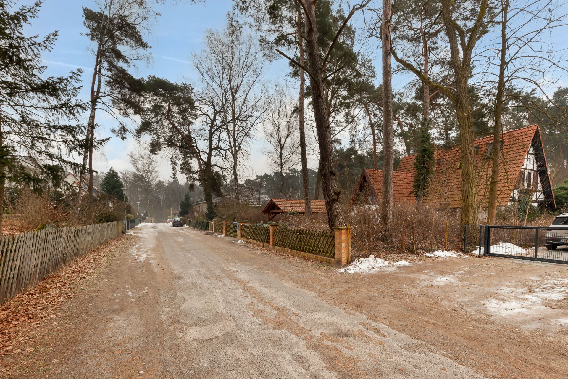 Ruhige Wohnstraße mit Bäumen, Holzzäunen und Häusern mit roten Dächern im Winter.