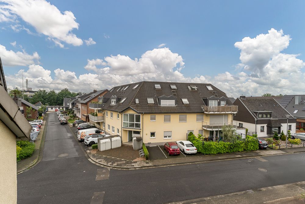 Mehrfamilienhaus mit dunklem Dach an einer ruhigen Wohnstraße, mehrere geparkte Autos davor.