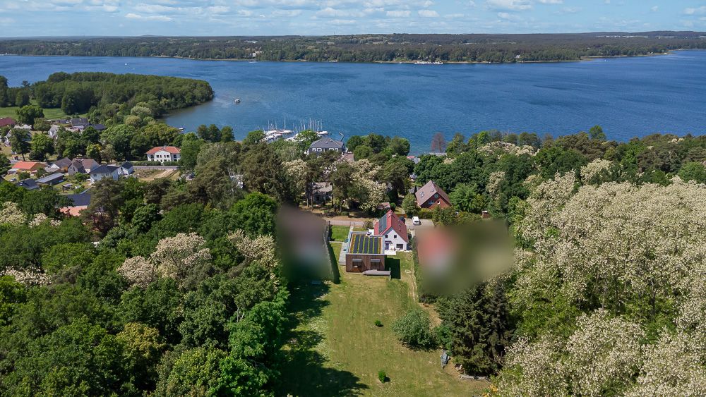 Luftaufnahme eines Hauses mit großem Garten und Blick auf einen See, umgeben von Bäumen.