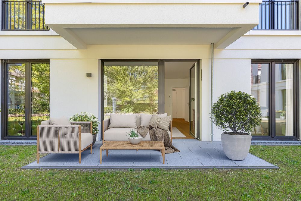 Moderne Terrasse mit Sofa, Sessel, Couchtisch und Pflanze vor einer Glastür zum Wohnbereich.