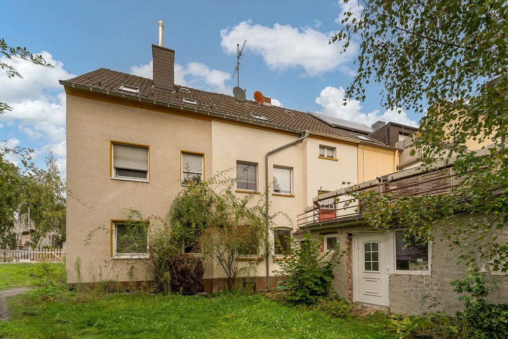 Rückansicht eines Wohnhauses mit Garten, Terrasse und mehreren Fenstern, umgeben von Pflanzen.