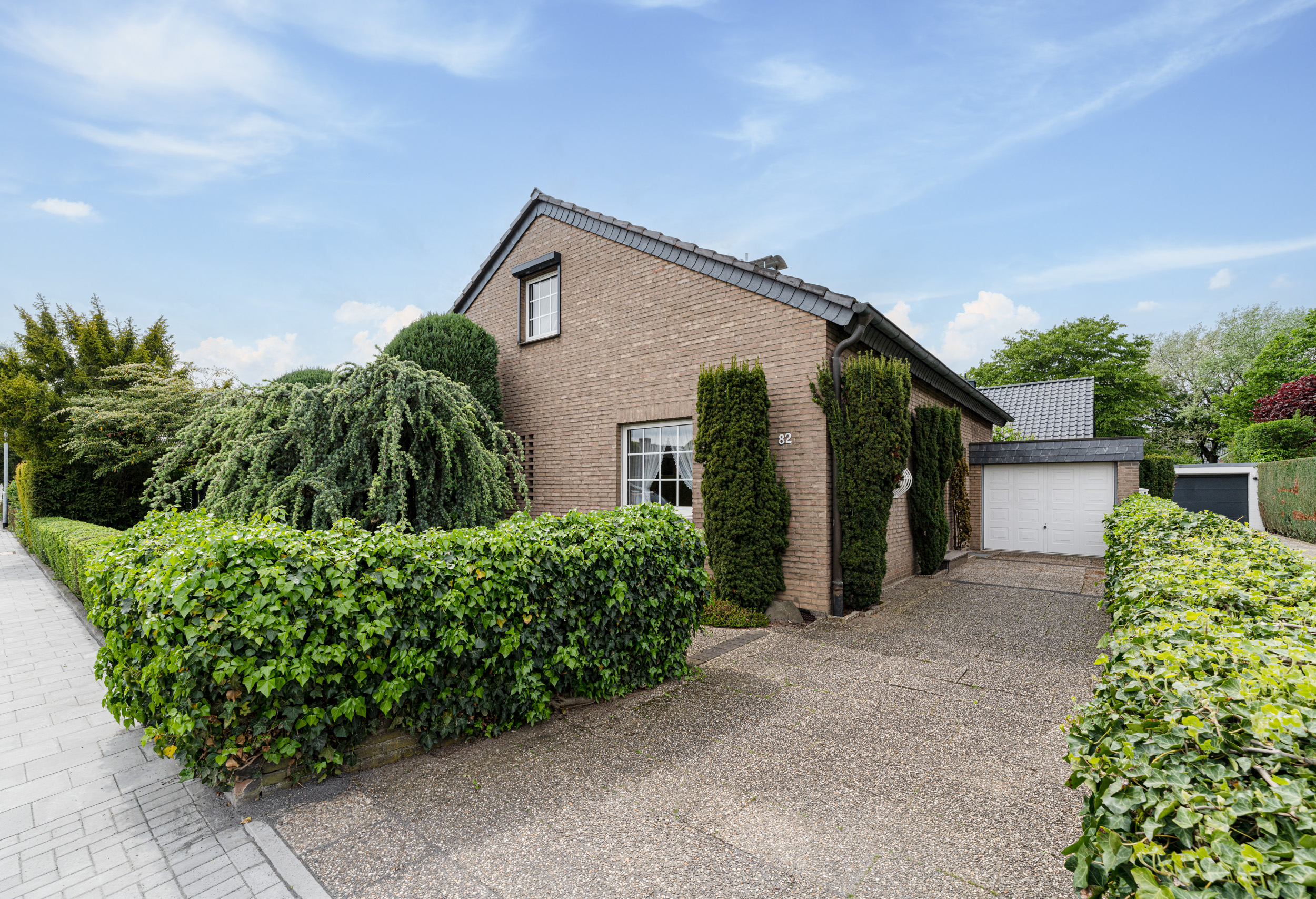 Einfamilienhaus mit Ziegelmauer, großer Garage und gepflegtem Garten mit Hecken.