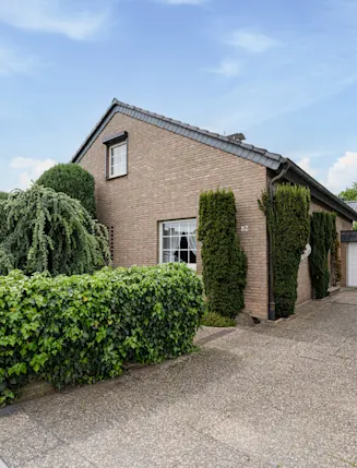 Einfamilienhaus mit Ziegelmauer, großer Garage und gepflegtem Garten mit Hecken.