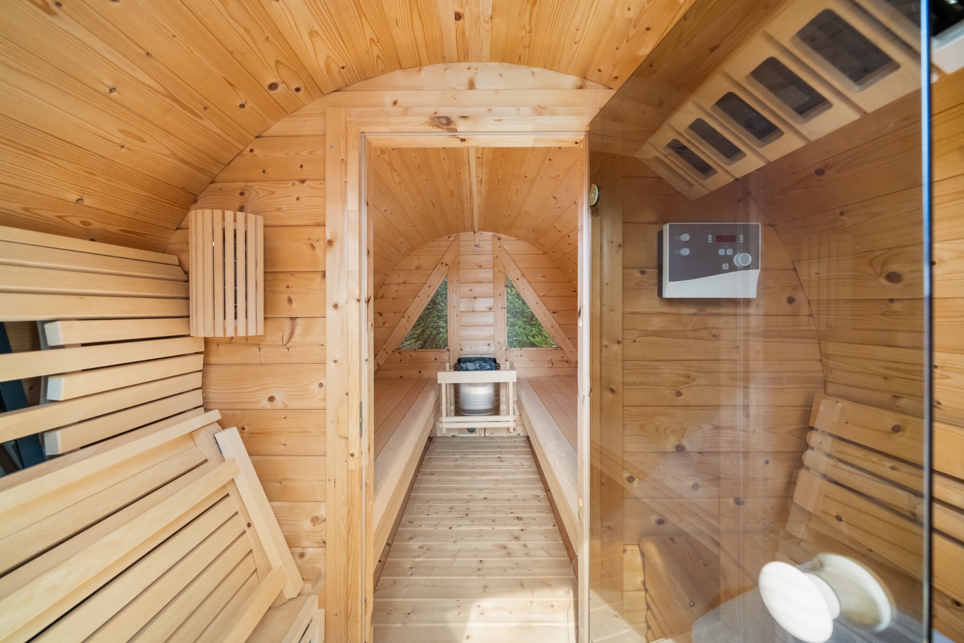 Innenansicht einer holzverkleideten Sauna mit Bänken und einem Saunaofen am Ende.