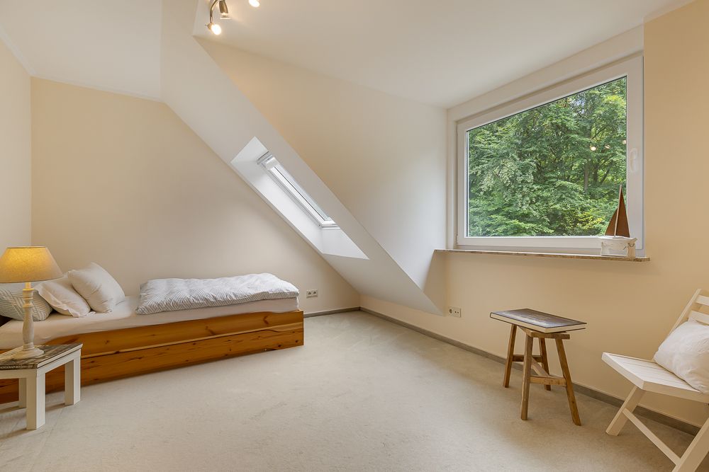 Helles Schlafzimmer mit Einzelbett, Fenster, kleinem Tisch und Stuhl.
