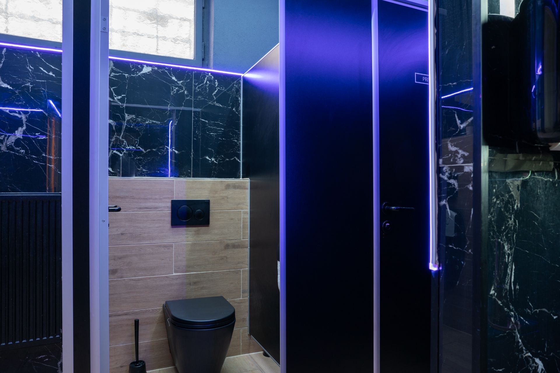 Modernes Bad mit schwarzer Toilette und Marmorfliesen, beleuchtet mit violettem LED-Licht.