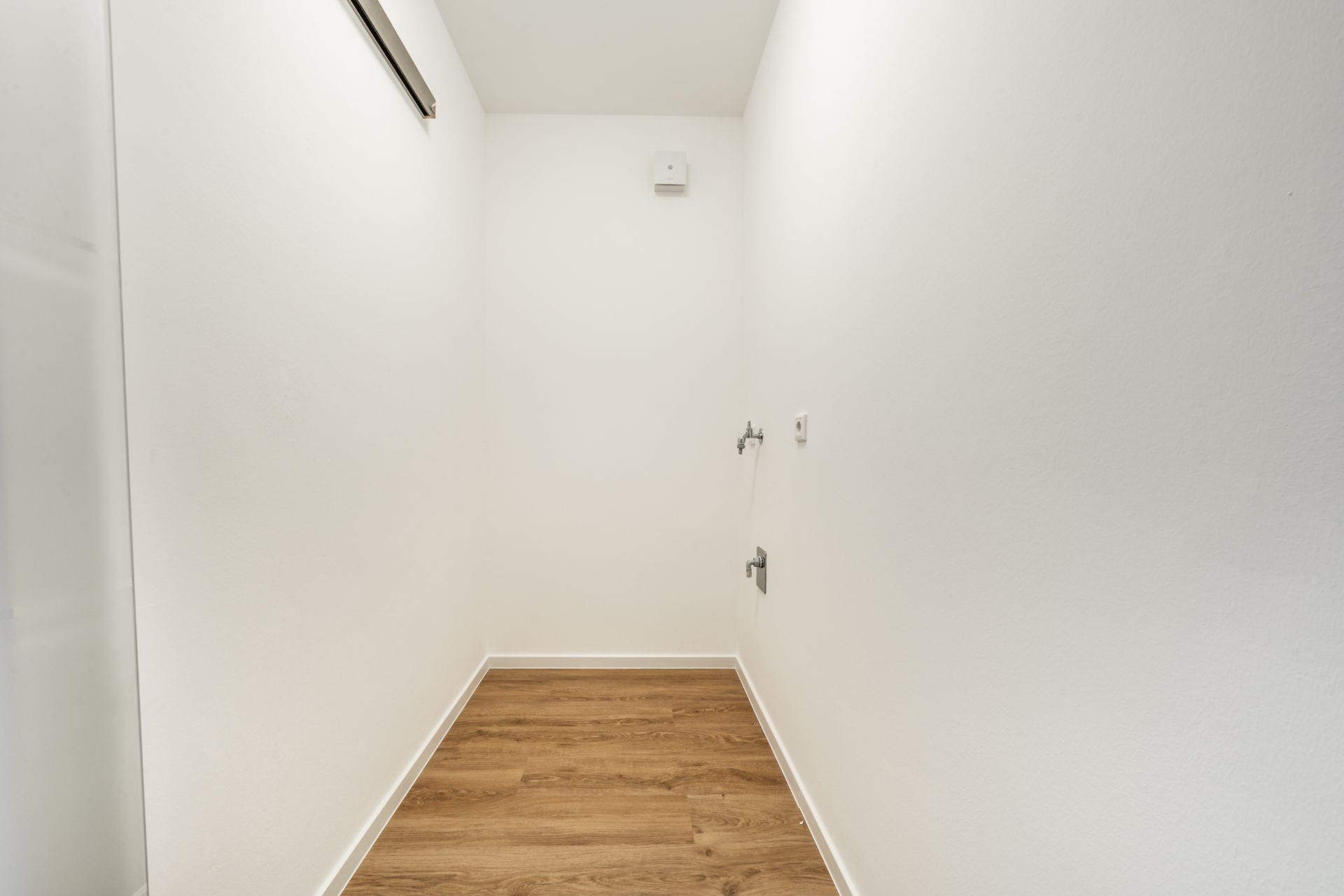 Schmaler, leerer Raum mit weiß gestrichenen Wänden und Holzfußboden.