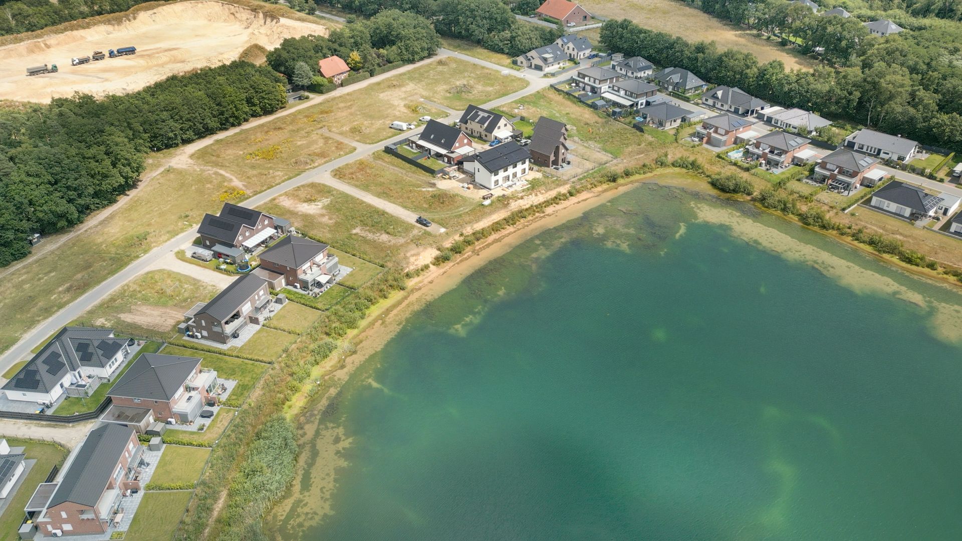 Luftaufnahme von Wohnhäusern an einem See mit Straßen und viel Grün.