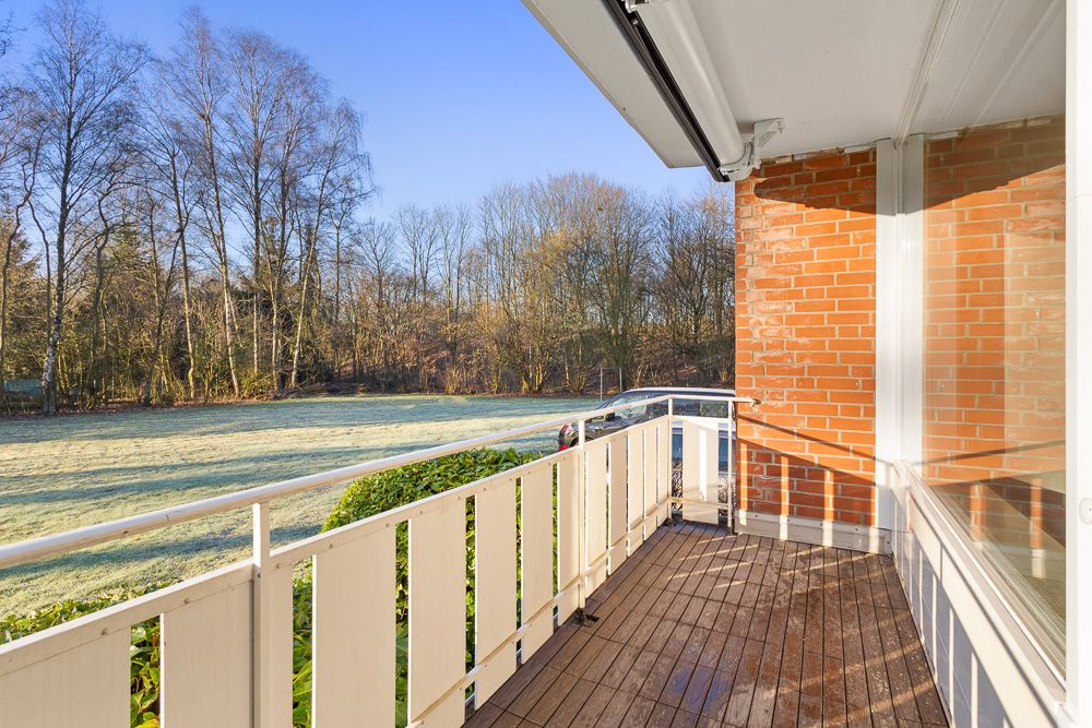 Holzbalkon mit weißem Geländer, Blick auf eine Wiese und Bäume im Hintergrund.