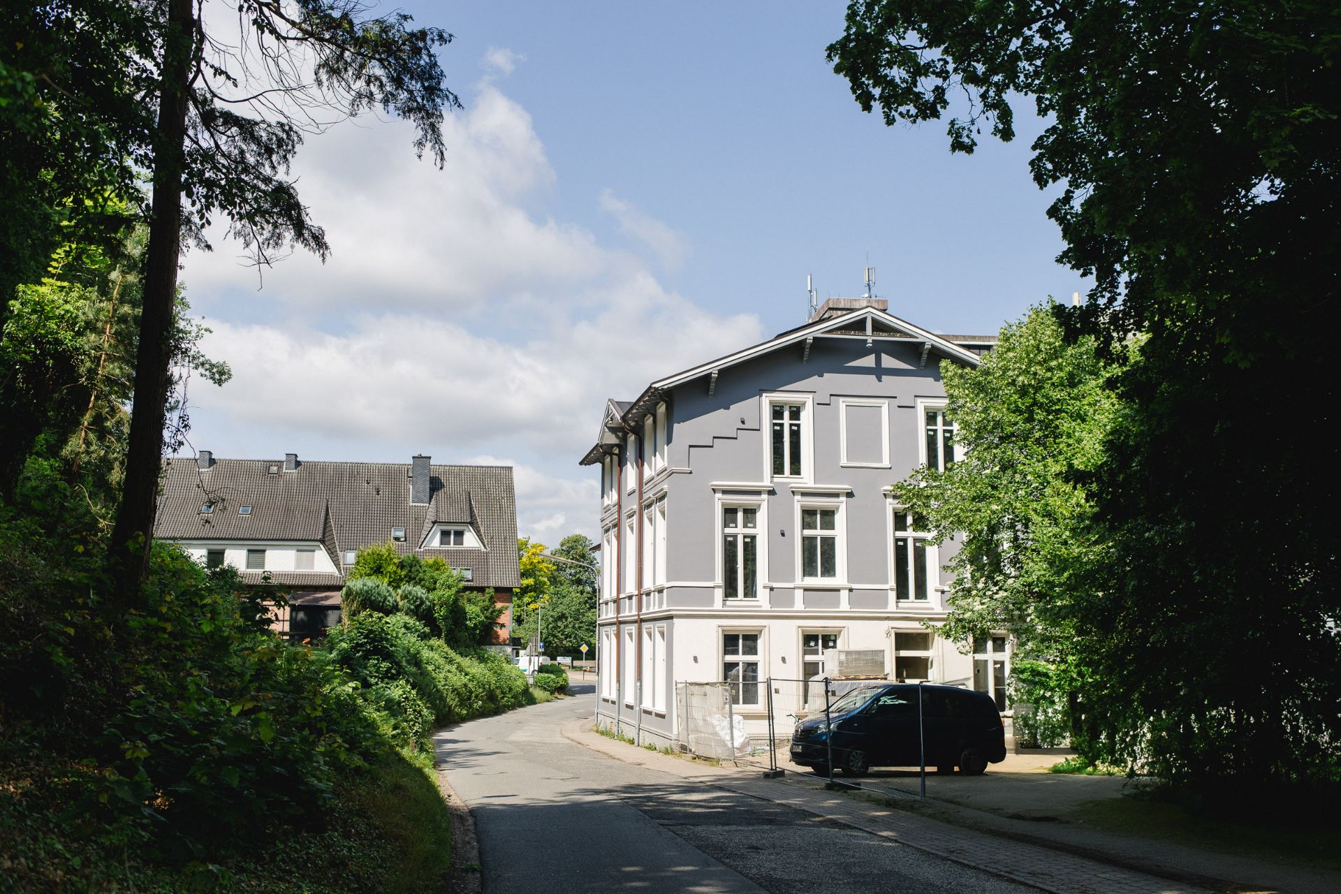 Wohnhaus mit grauer Fassade an einer ruhigen Straße, umgeben von Bäumen.