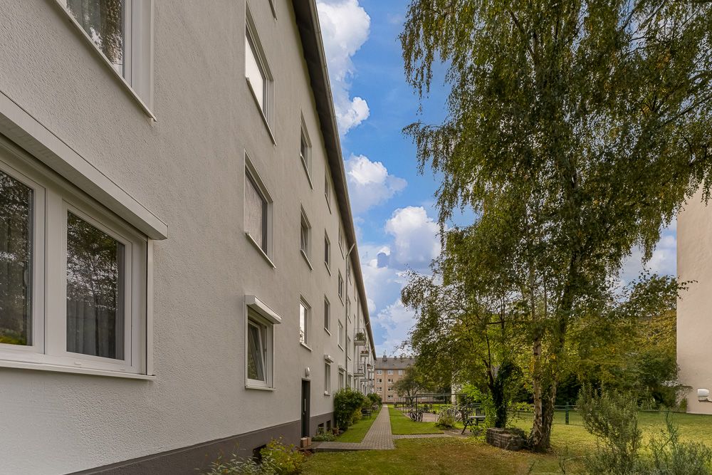 Langes Wohngebäude mit Garten und Bäumen an der Seite unter blauem Himmel.
