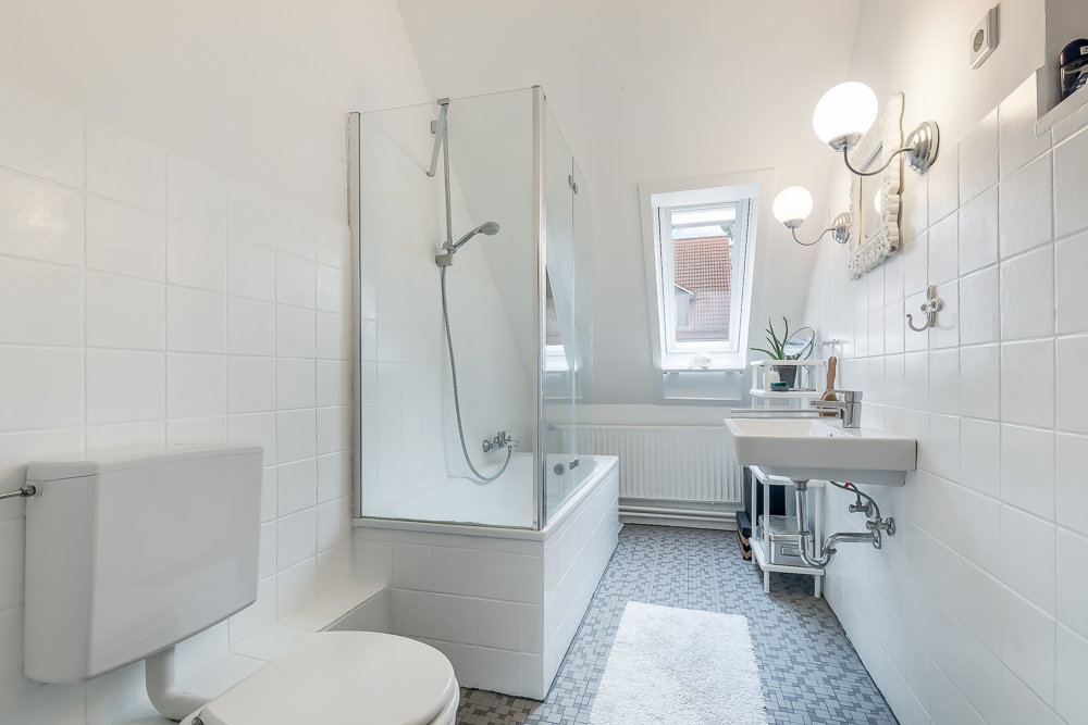 Helles Badezimmer mit Badewanne, WC, Waschbecken und zwei Fenstern.
