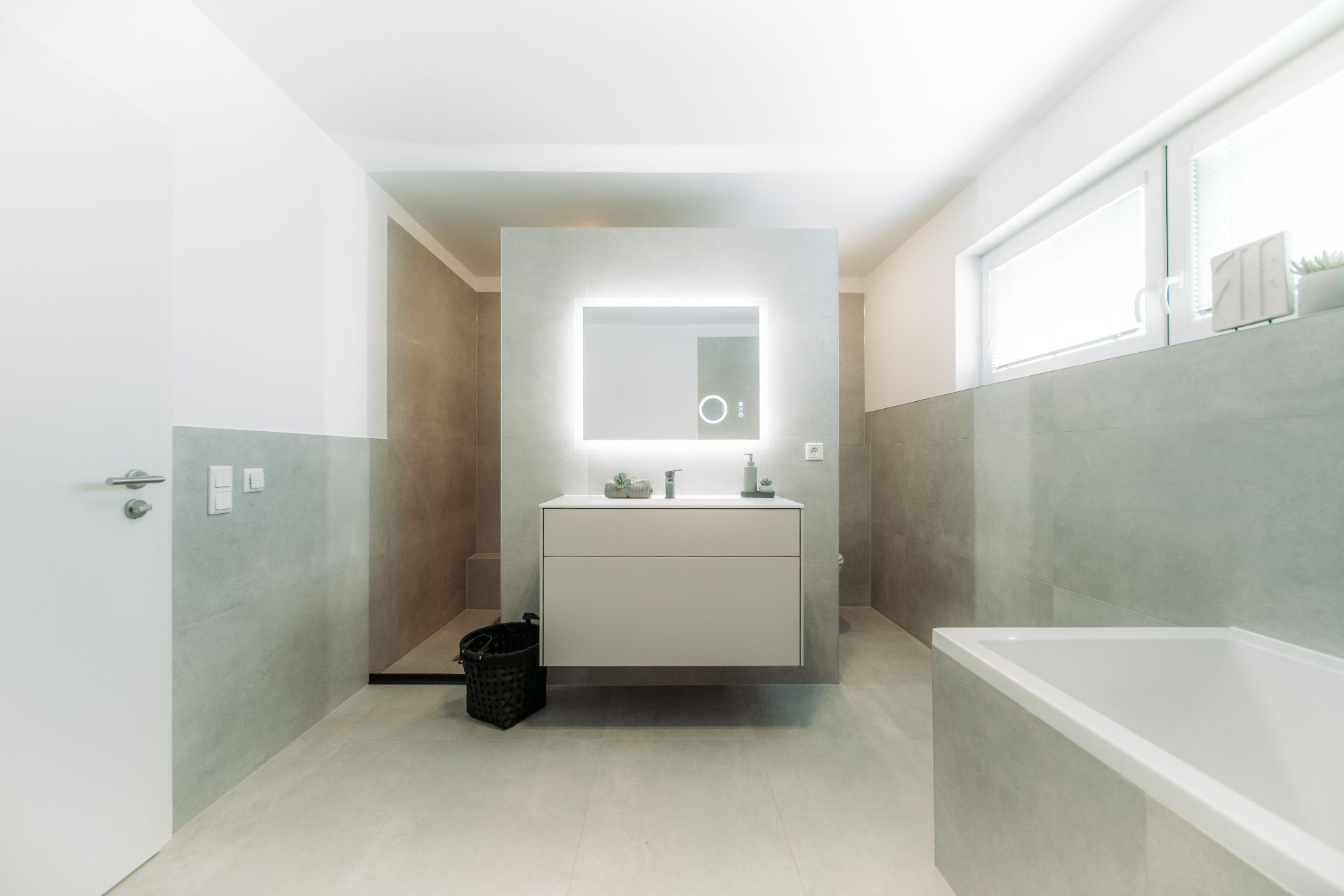 Modernes Badezimmer mit Waschtisch, beleuchtetem Spiegel, Badewanne und Dusche.