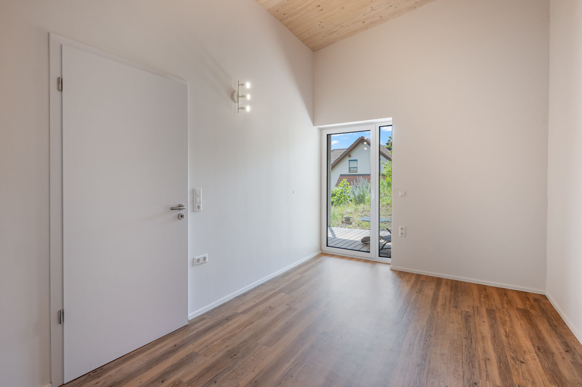 Leerer Raum mit Holzboden, weißer Tür und Glastür zum Garten.