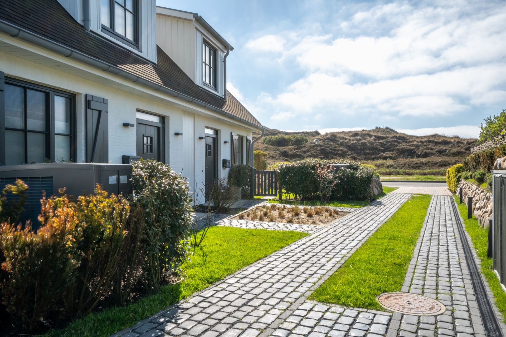 Gepflasterter Weg und Garten vor einem weißen Wohnhaus mit mehreren Eingängen.