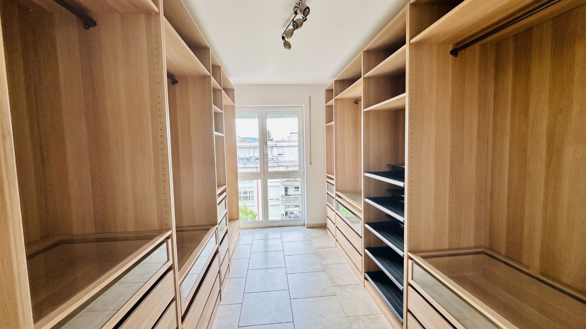 Begehbarer Kleiderschrank mit Holzregalen, Schubladen und Fenster am Ende des Raums.
