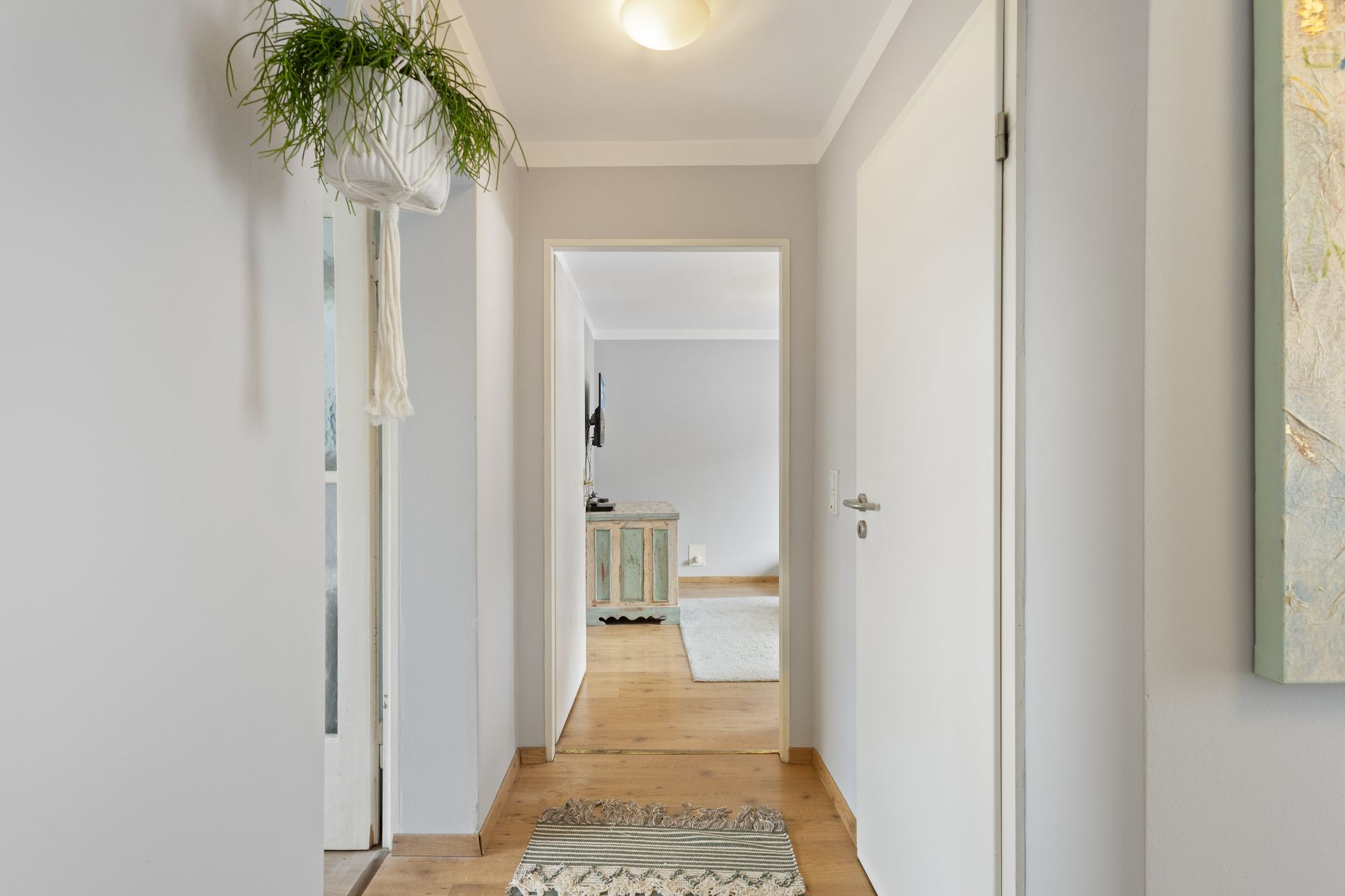 Heller Flur mit Holzboden, Hängepflanze und Blick in ein weiteres Zimmer.