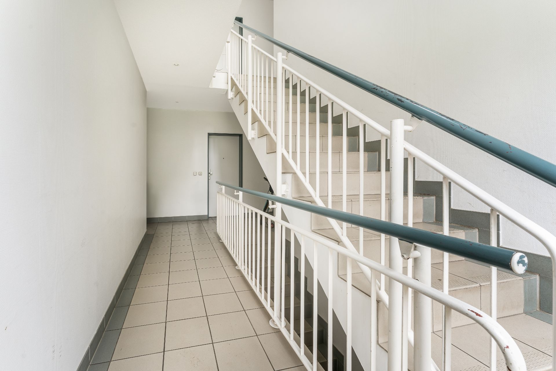 Heller Treppenhausflur mit gefliesten Böden und weißen Wänden in einem Wohngebäude.