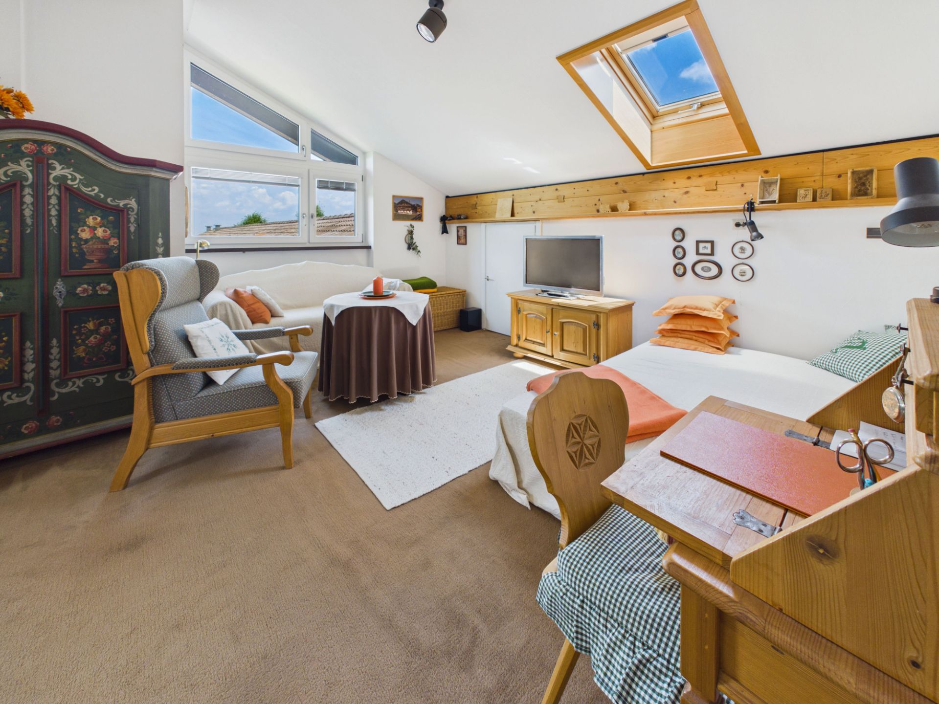 Helles Zimmer mit Bett, Schreibtisch, TV, Sessel, Esstisch und Oberlichtfenster.