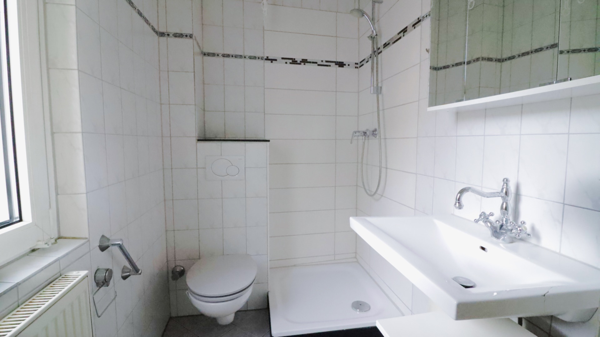 Kleines, weiß gefliestes Badezimmer mit Dusche, Wandtoilette und Waschbecken.