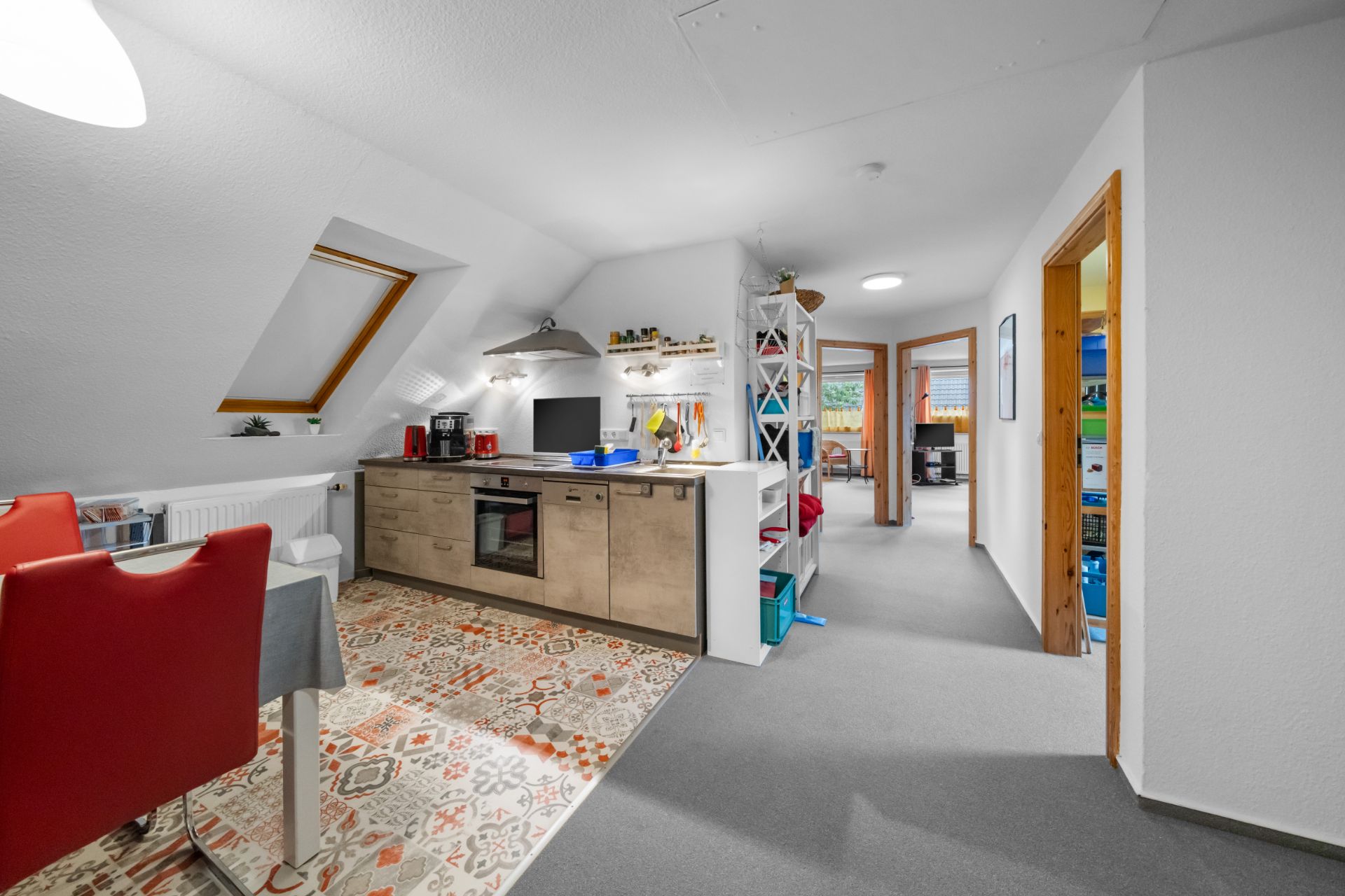 Moderne Küche mit Dachfenster, rotem Essbereich und Regalen, Blick auf angrenzende Zimmer.