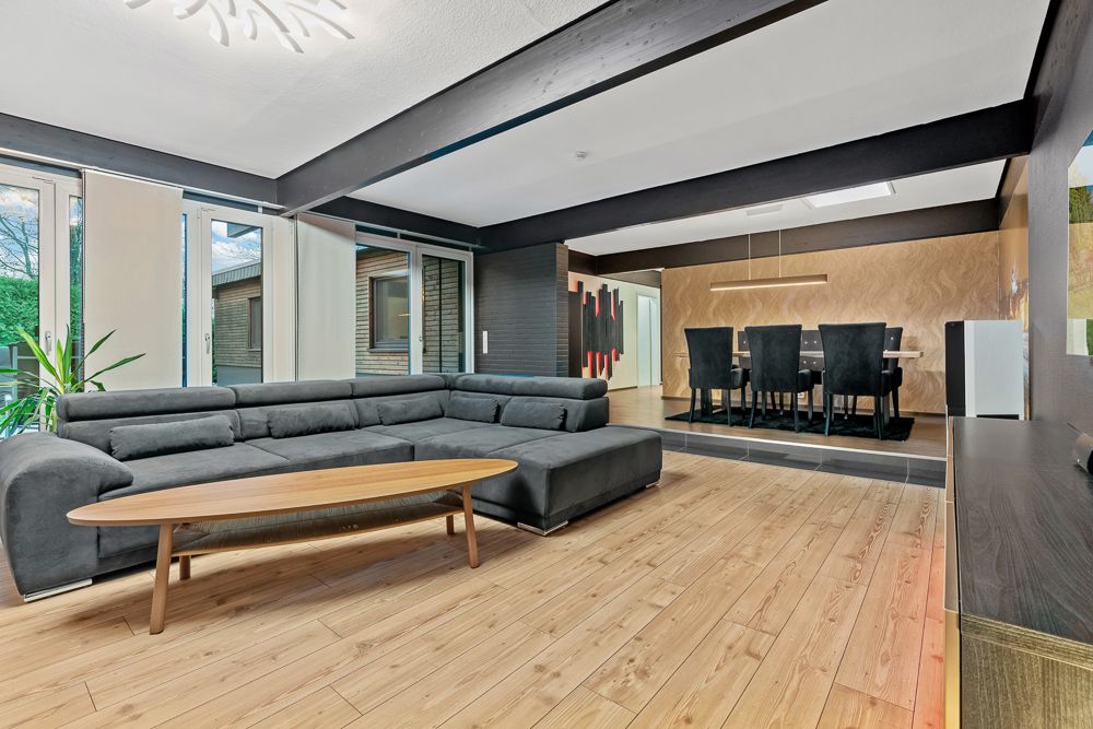 Modernes Wohnzimmer mit grauem Ecksofa, Holz-Couchtisch und offenem Essbereich im Hintergrund.