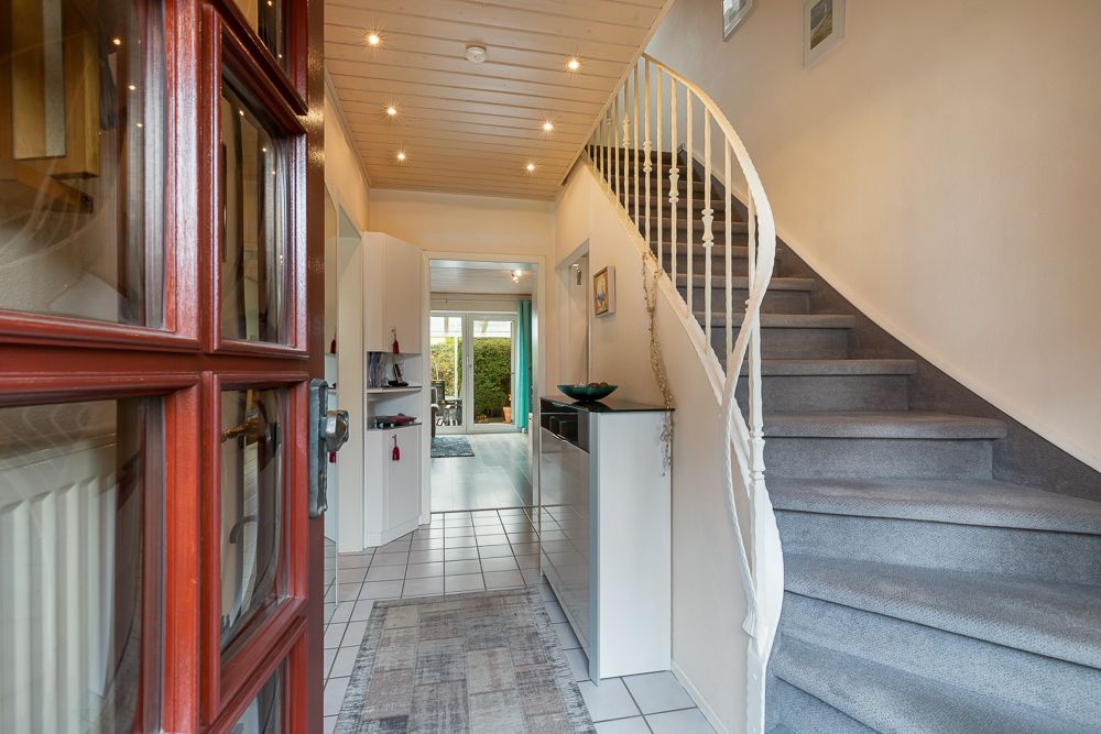 Flur mit offenstehender Haustür, Teppichtreppe und Blick ins Wohnzimmer.