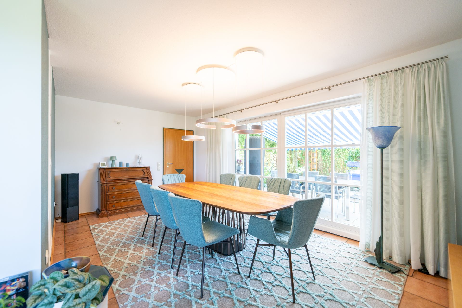 Helles Esszimmer mit großem Holztisch, acht Stühlen und großen Fenstern mit Vorhängen.