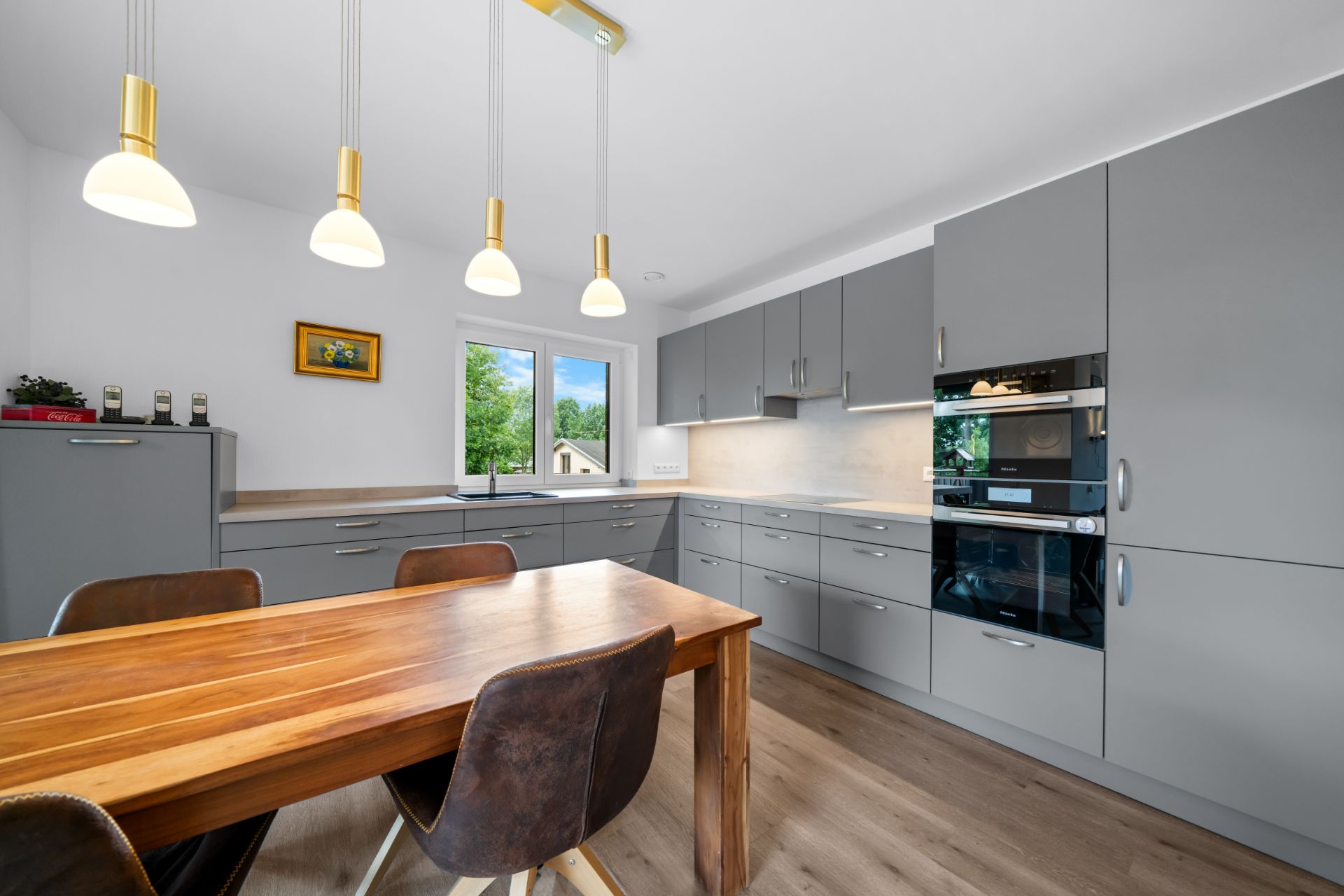 Moderne Küche mit grauen Schränken, Holz-Esstisch, vier Stühlen und Hängelampen.