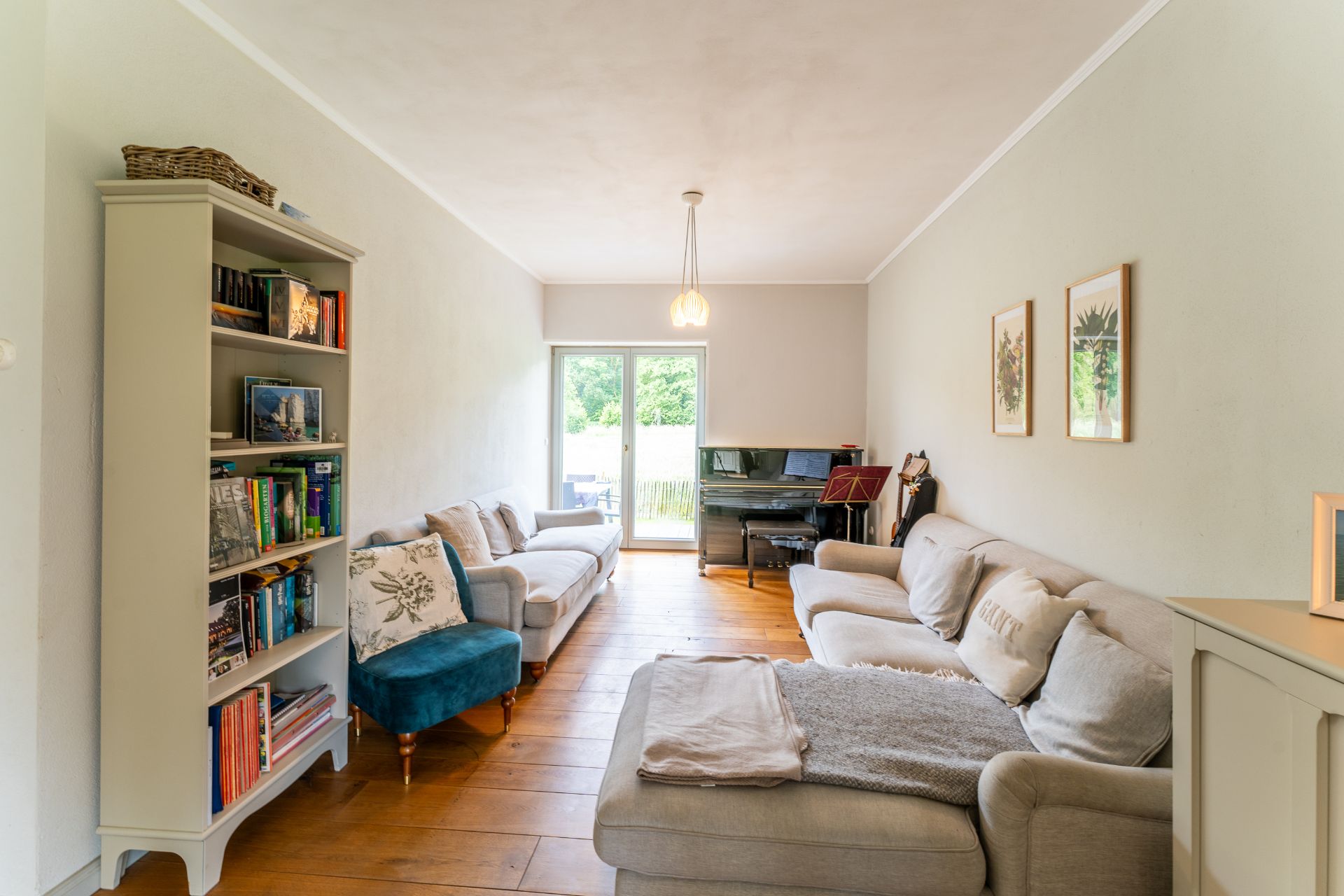 Helles Wohnzimmer mit Sofas, Bücherregal, Klavier und Zugang zu einer Terrasse.