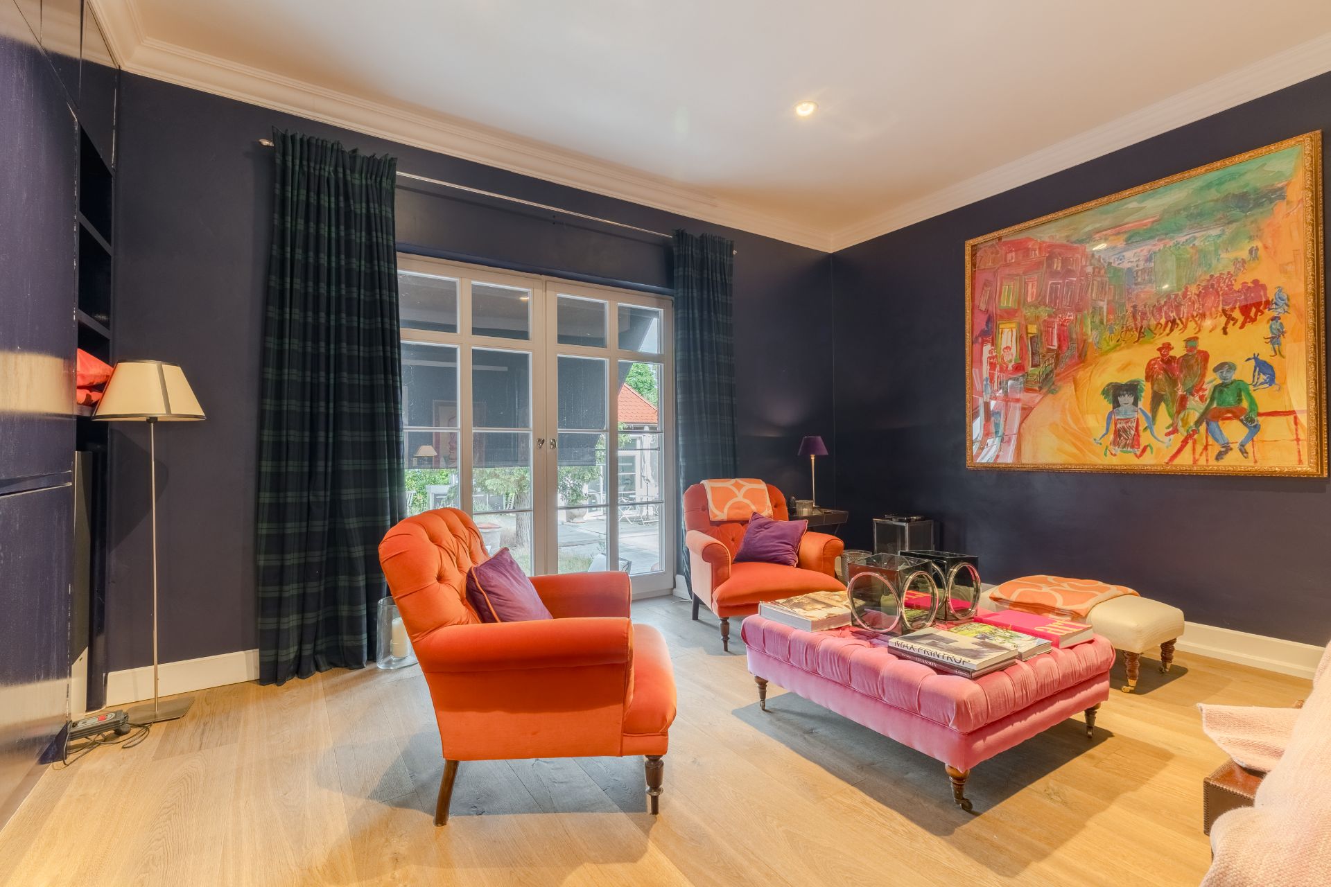 Wohnzimmer mit orangefarbenen Sesseln, großem Gemälde, Couchtisch und Glastür zum Garten.