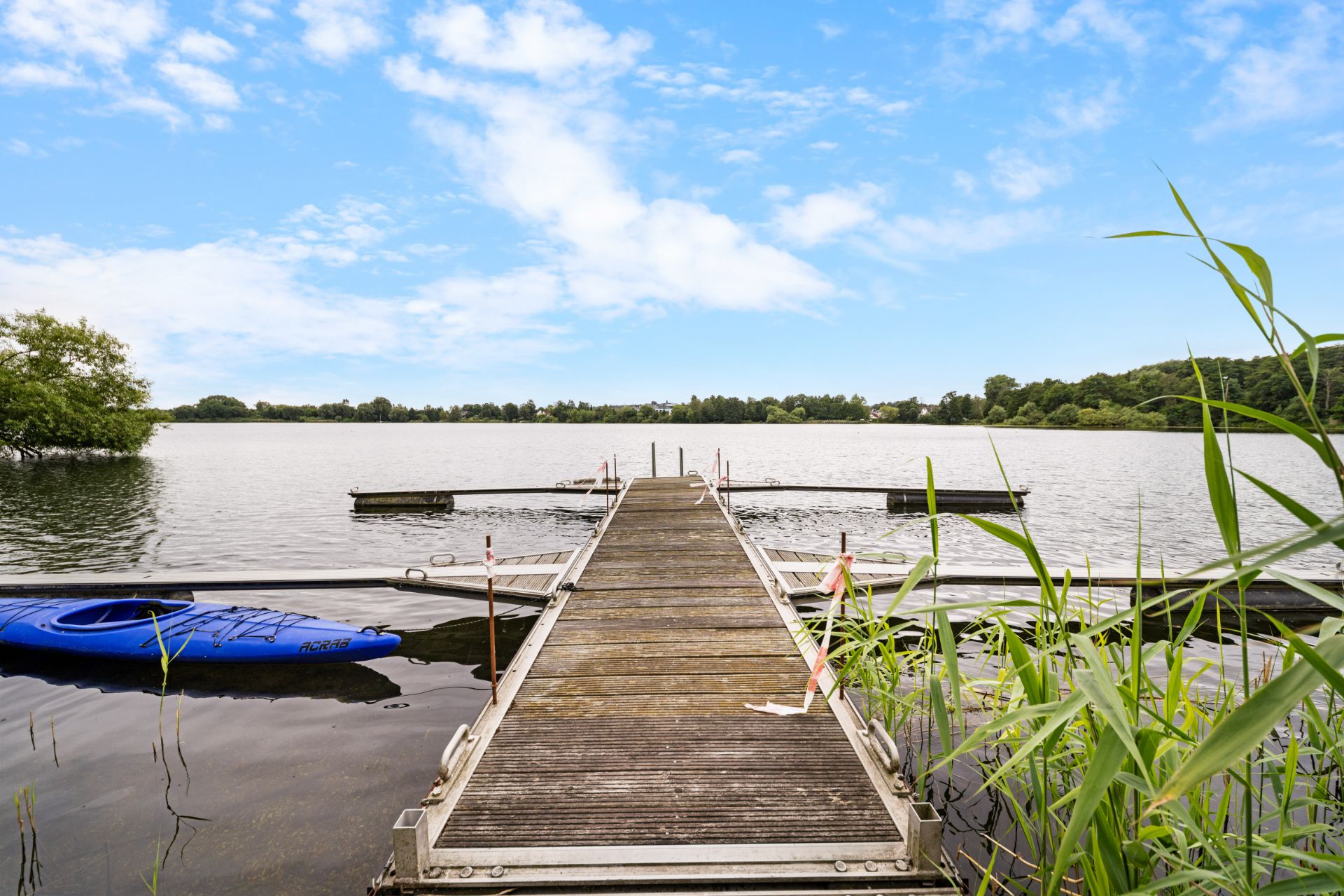 Holzsteg führt auf einen ruhigen See, links liegt ein blaues Kajak im Wasser.